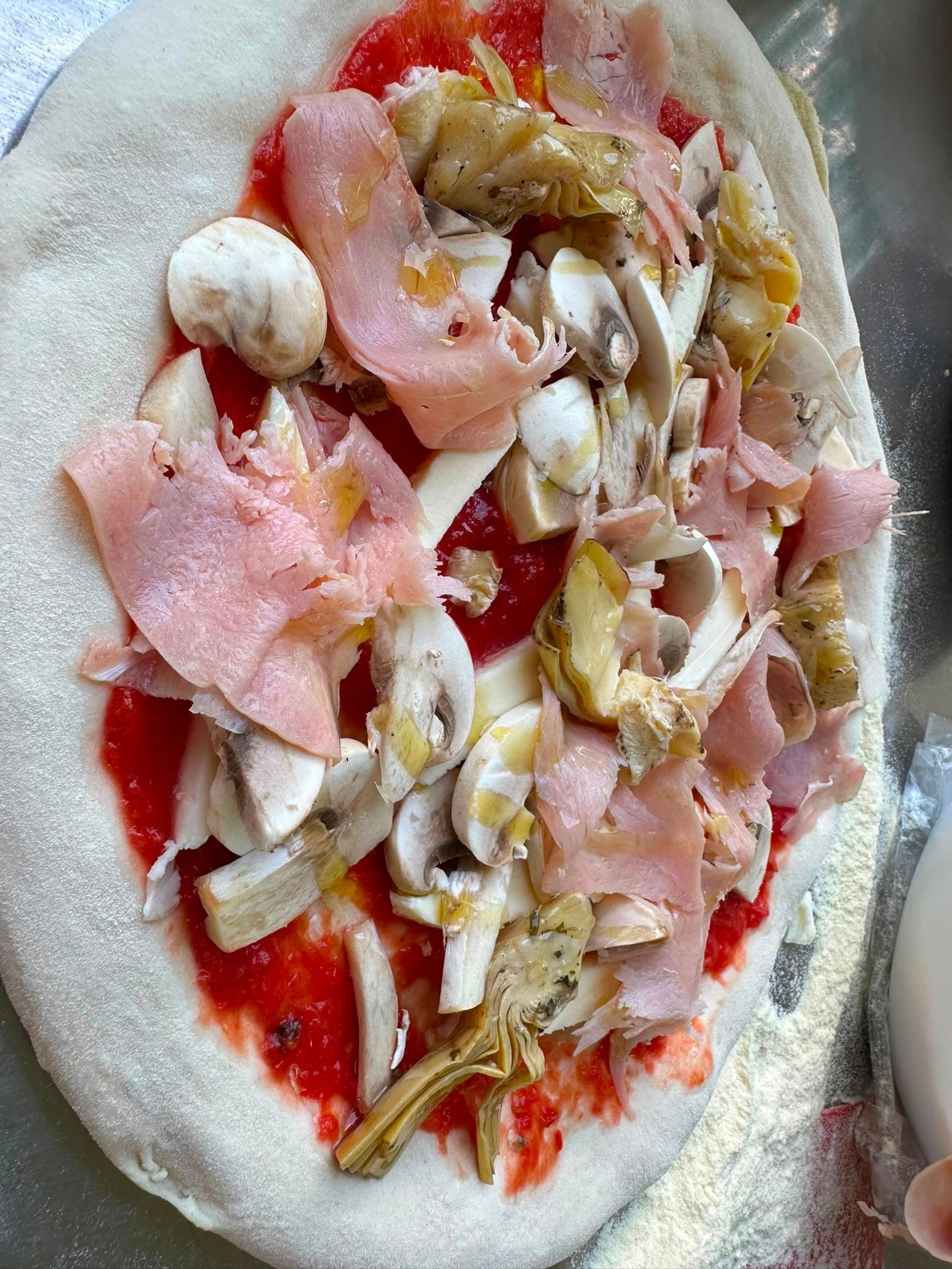 Pizza bei der Vorbereitung mit Schinken, Pilzen und Artischocken